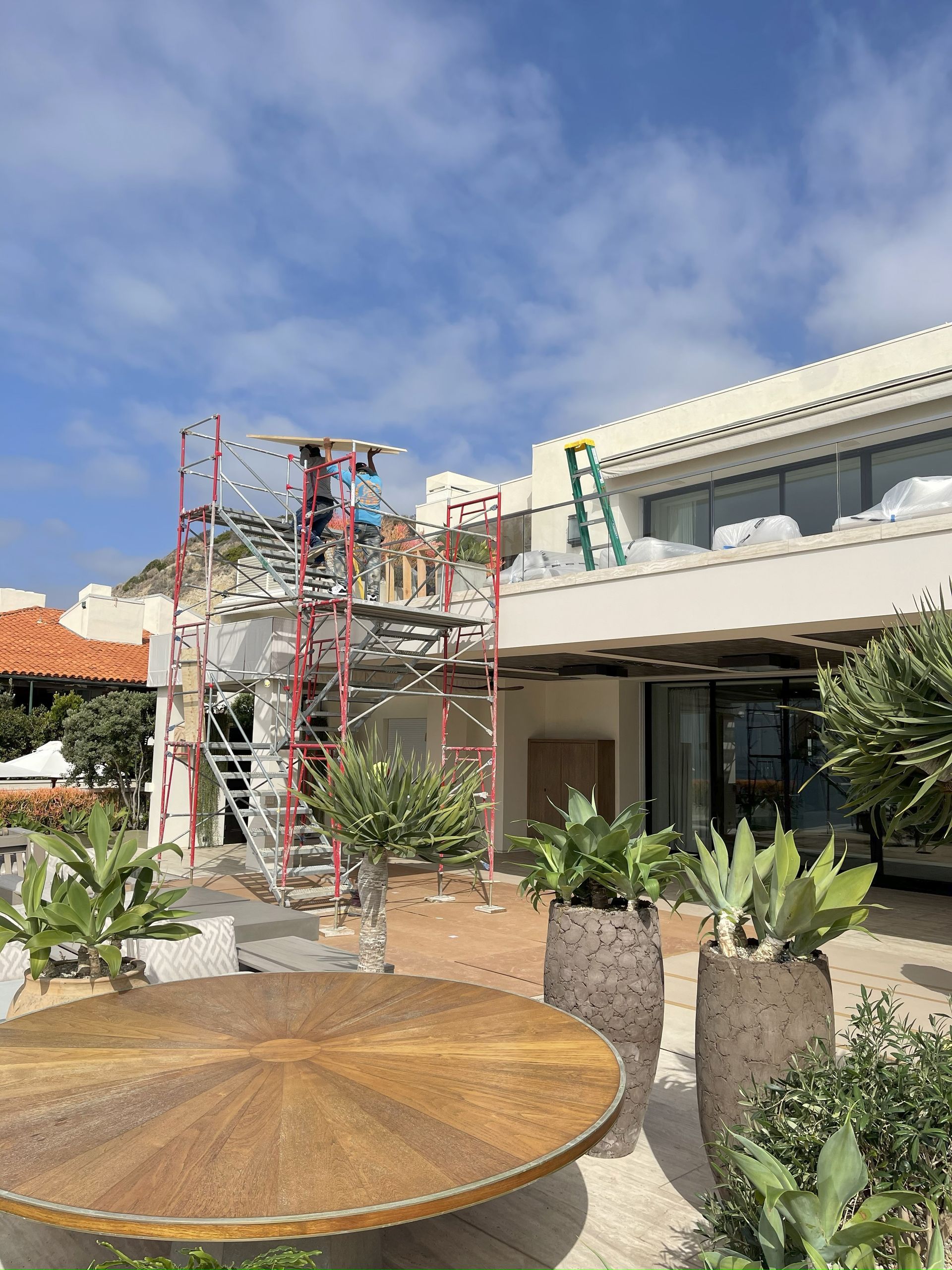 Construction on a white building, scaffolding in place. A ladder on the roof. Sunny day, blue sky.