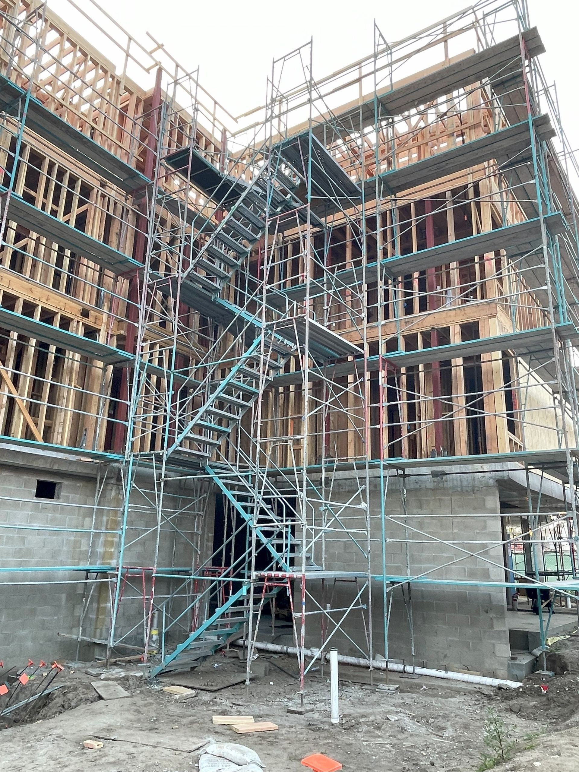 Construction site with scaffolding surrounding a multi-story wooden framed building.