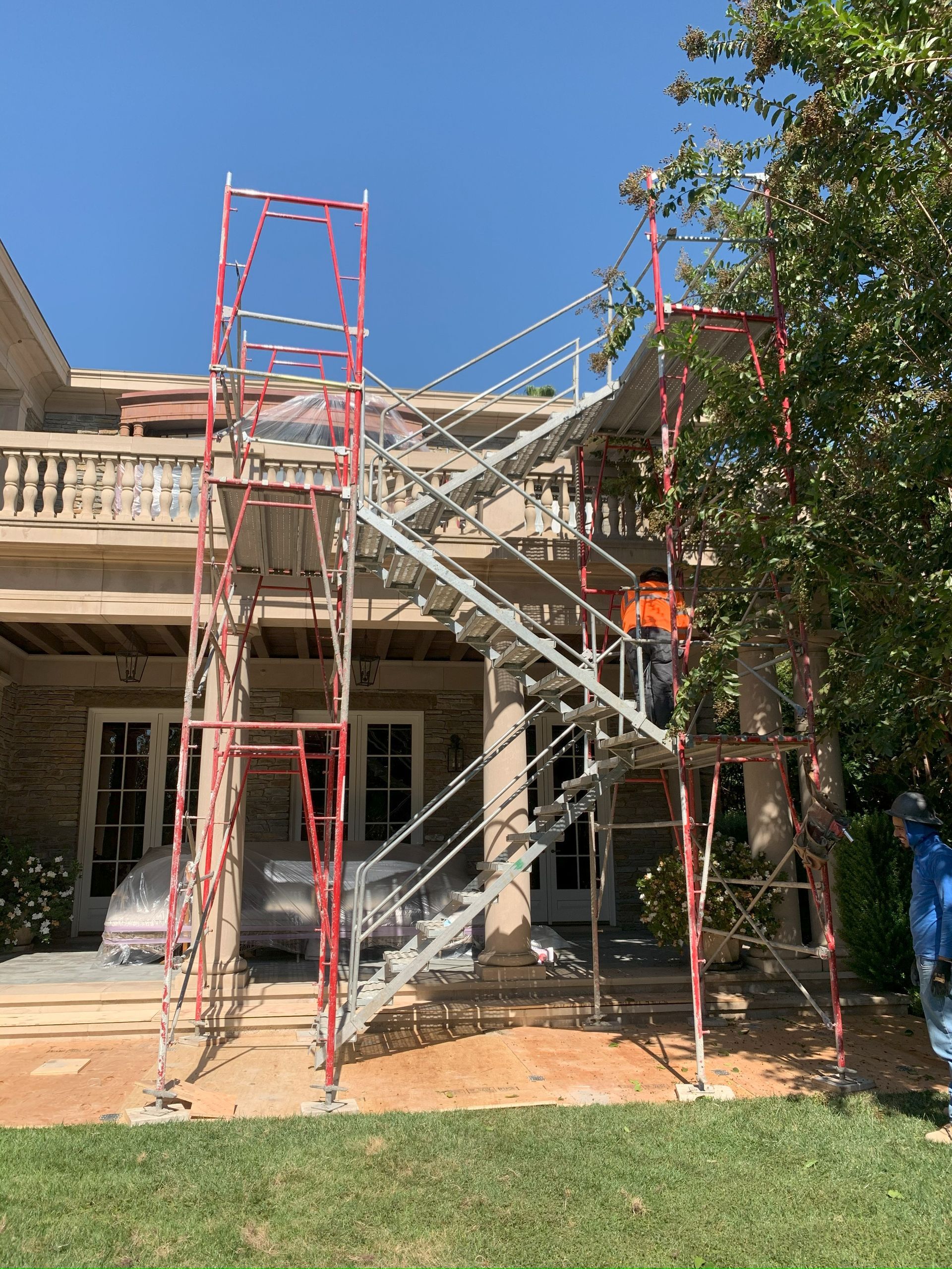 Red scaffolding with stairs built on a porch for construction work; a person is working.