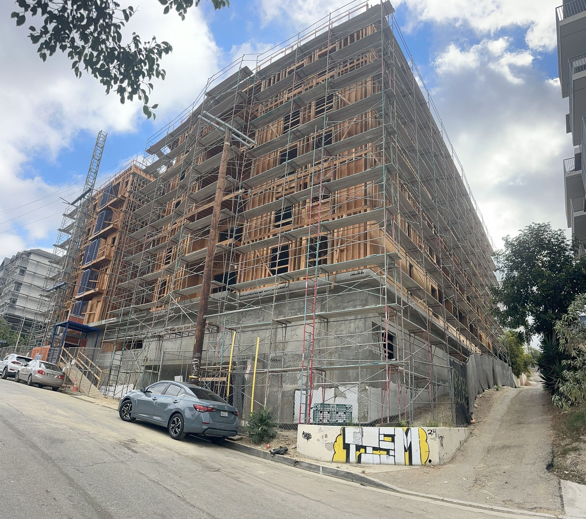 Multi-story building under construction with scaffolding. Gray car parked on a sloping street.