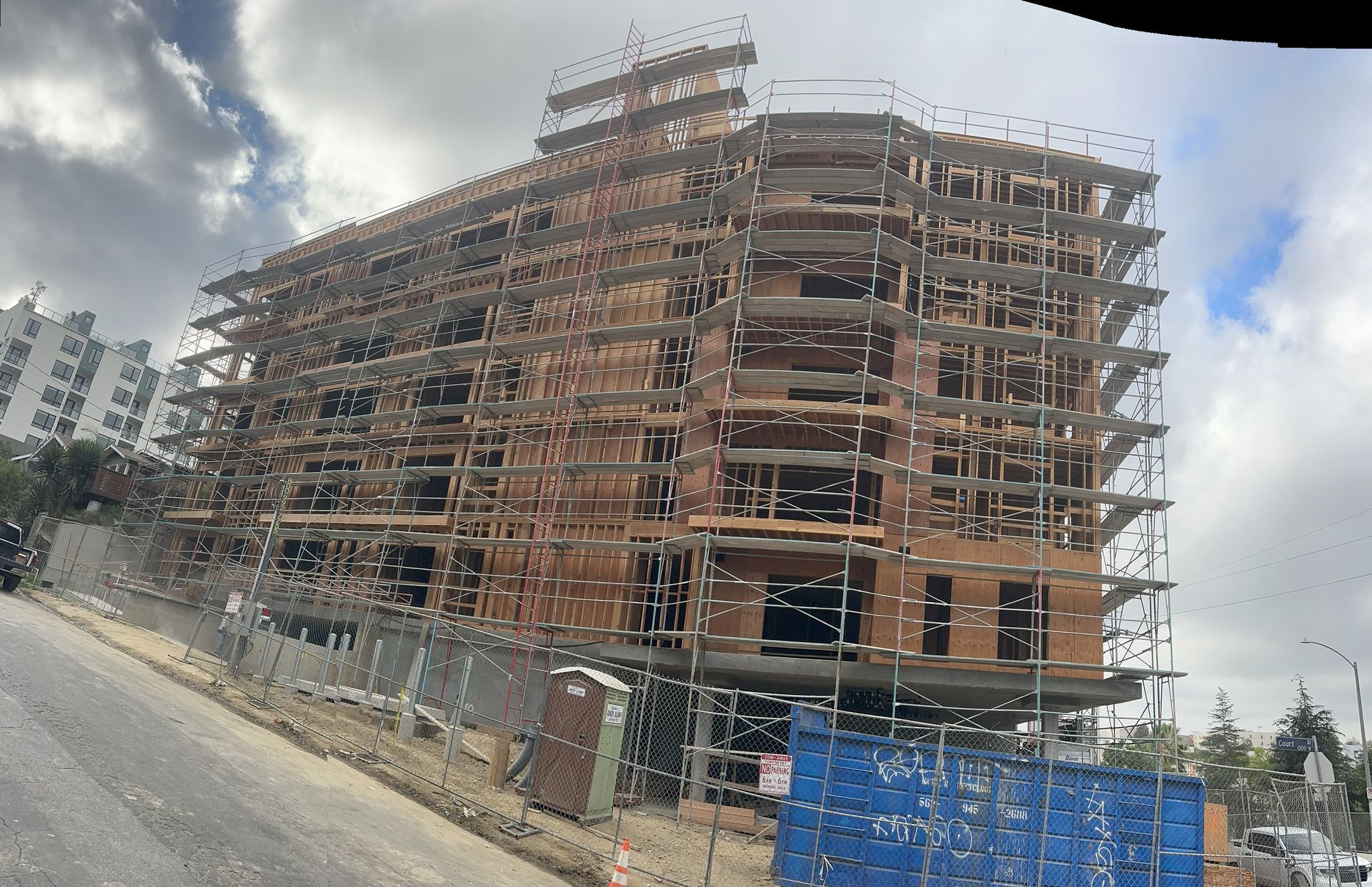 Building under construction, with wooden scaffolding and framing, set on a hillside with a cloudy sky.