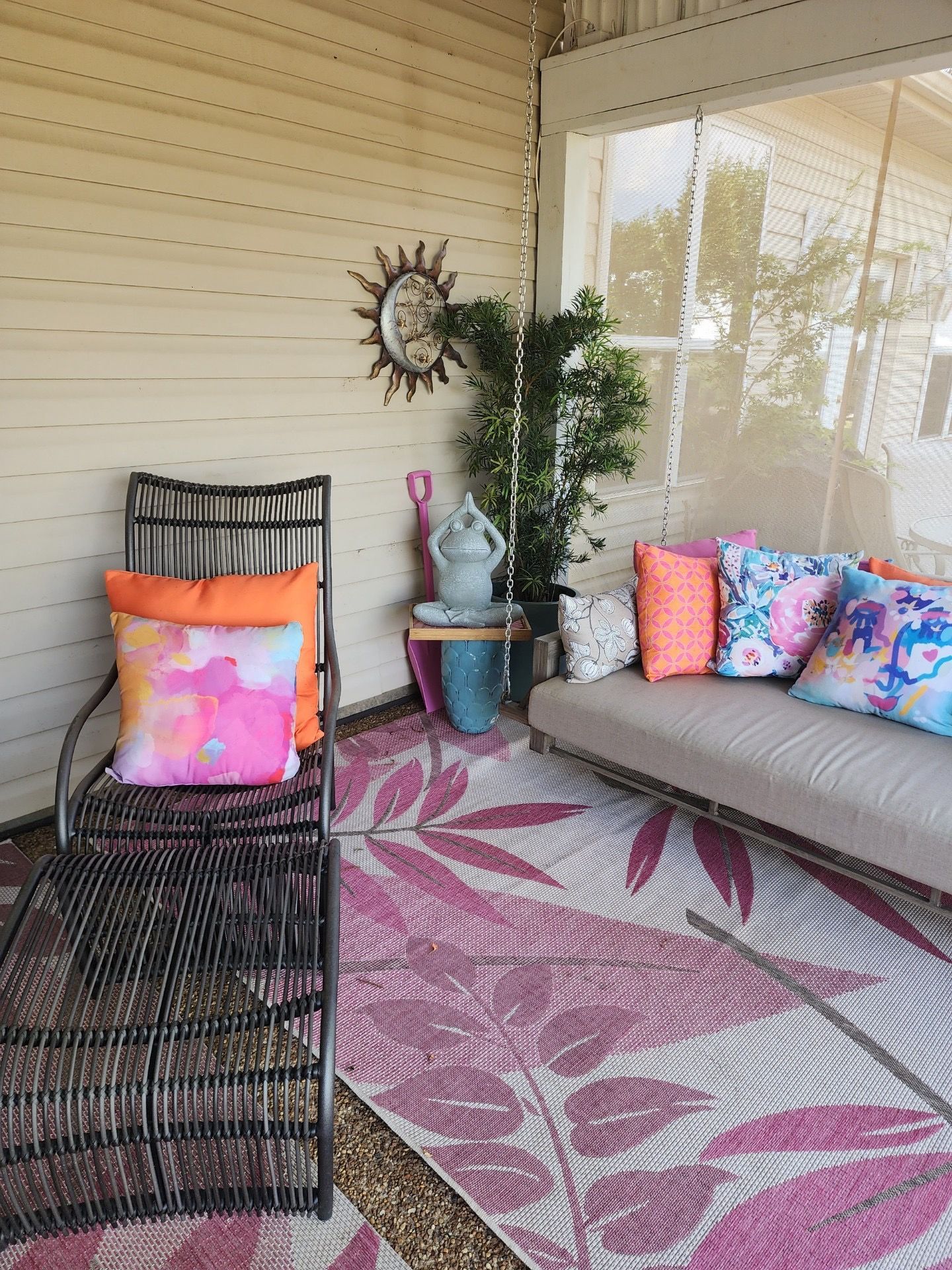 Outdoor seating area with lounge chair, sofa, decorative pillows, sunburst mirror, and floral rug.