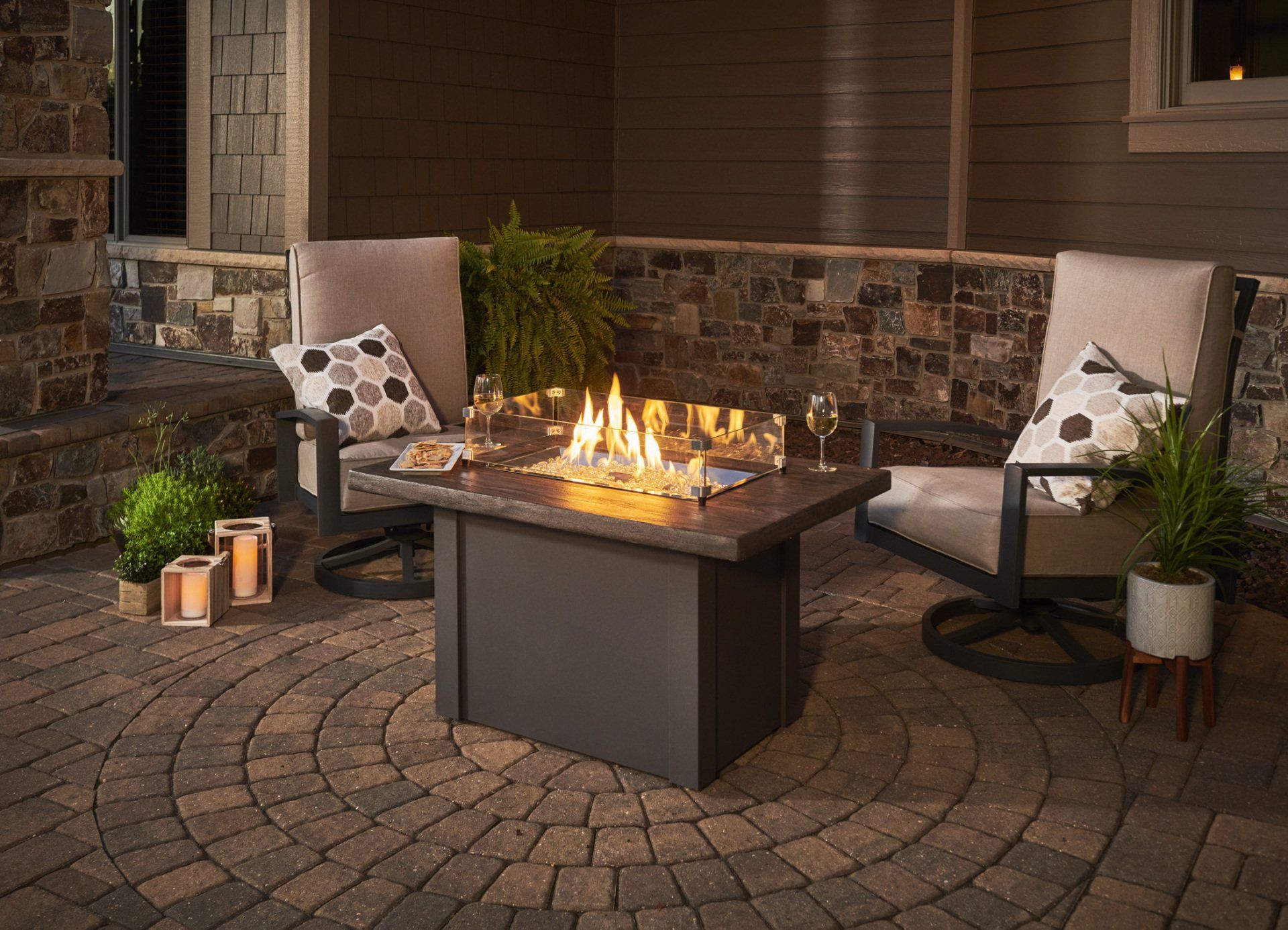 Outdoor patio with a lit fire pit, two chairs, and plants.