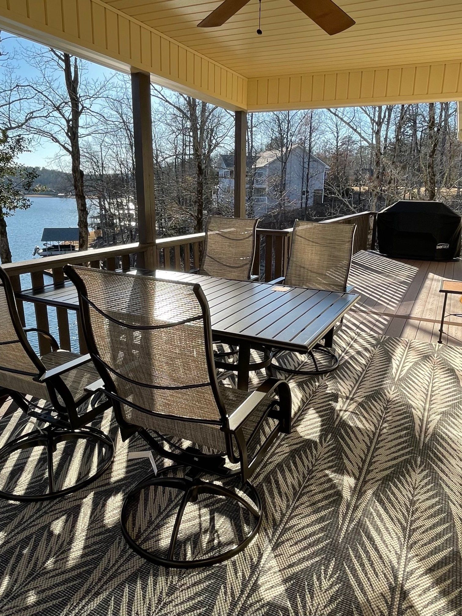 Outdoor deck with patio furniture, overlooking a lake and trees on a sunny day.