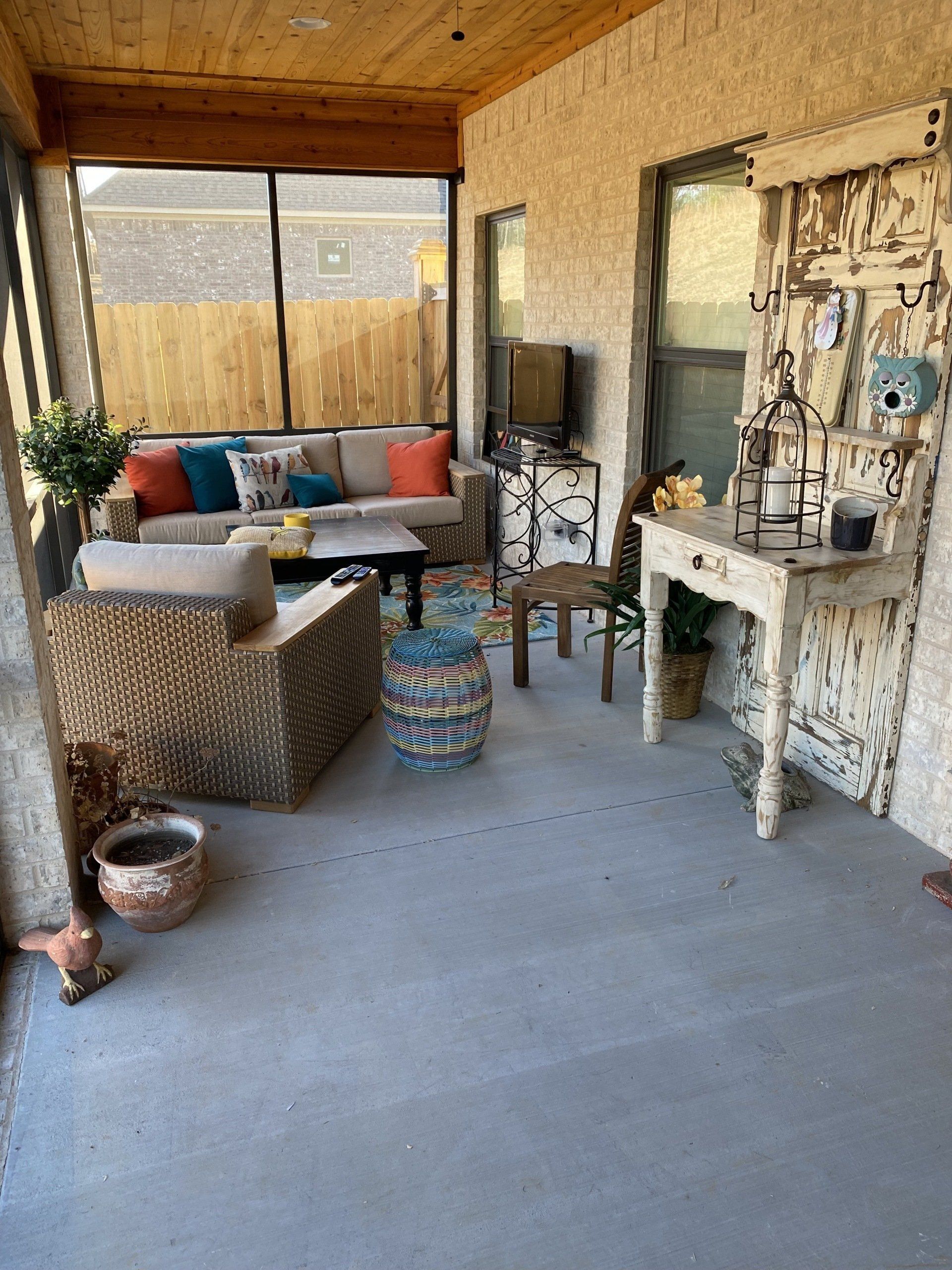 Cozy screened porch with outdoor furniture, including a sofa, chairs, and a small table. Beige, blue, and brown colors.