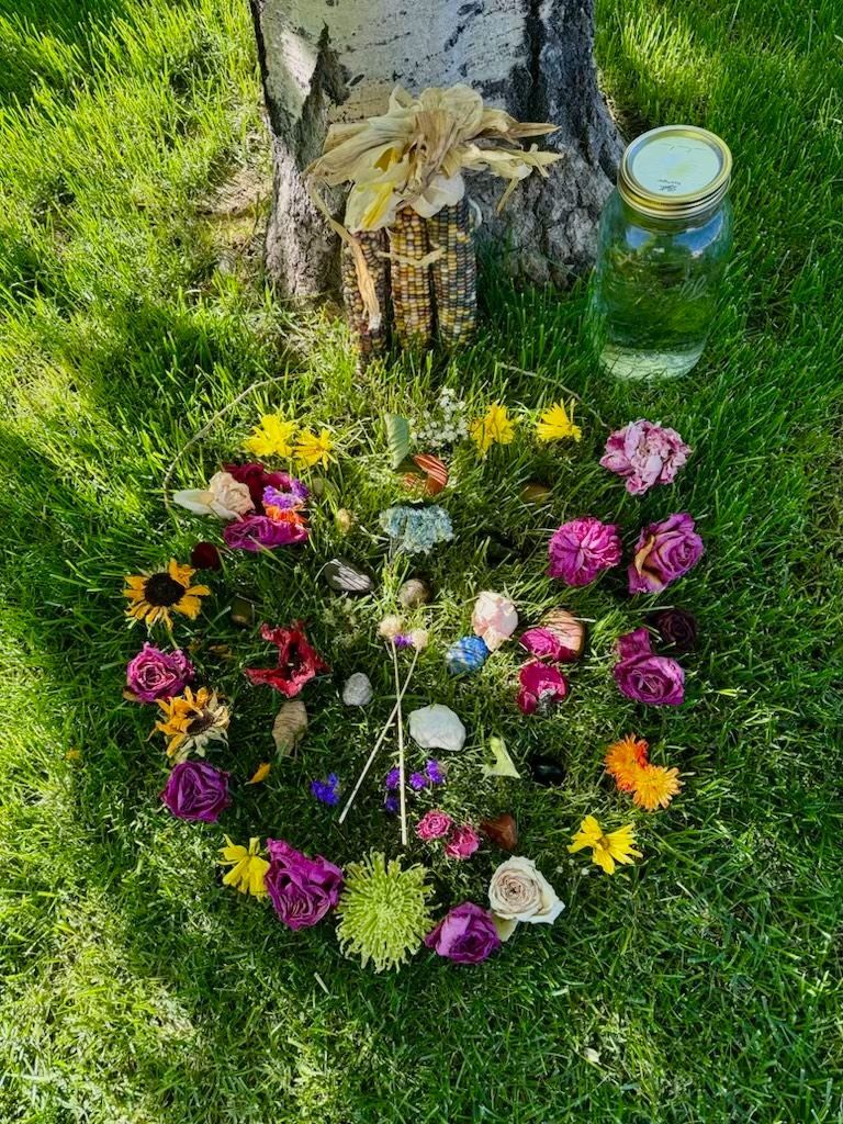 A circle of flowers and rocks in the grass next to a tree.