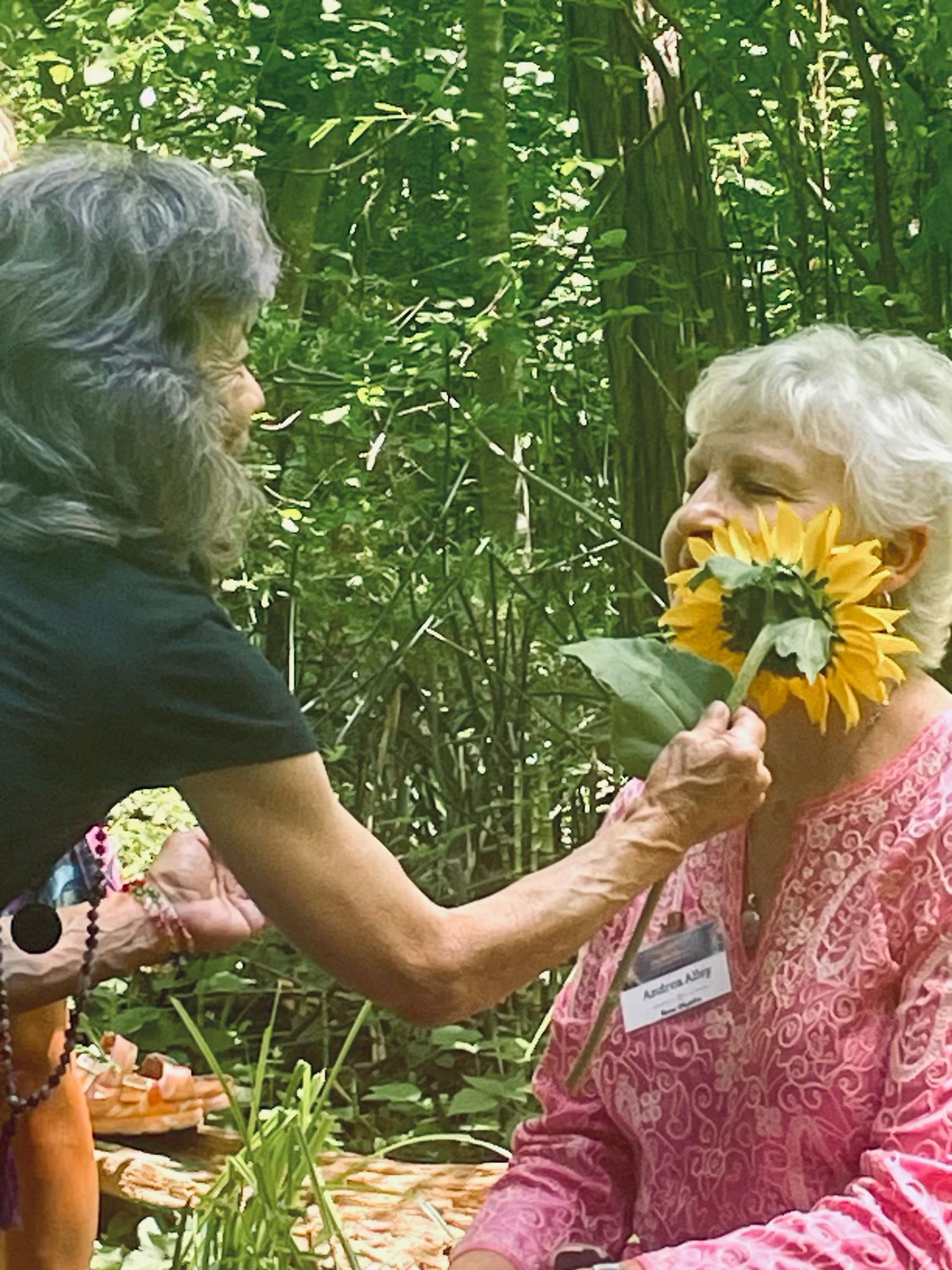 A woman is holding a sunflower in front of another woman 's face.