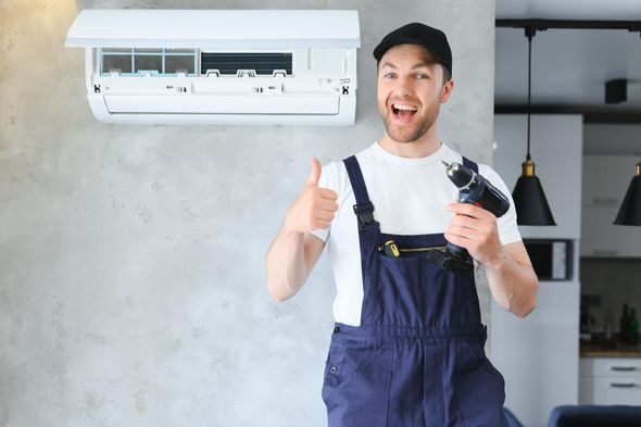 A man is holding a drill and giving a thumbs up in front of an air conditioner.