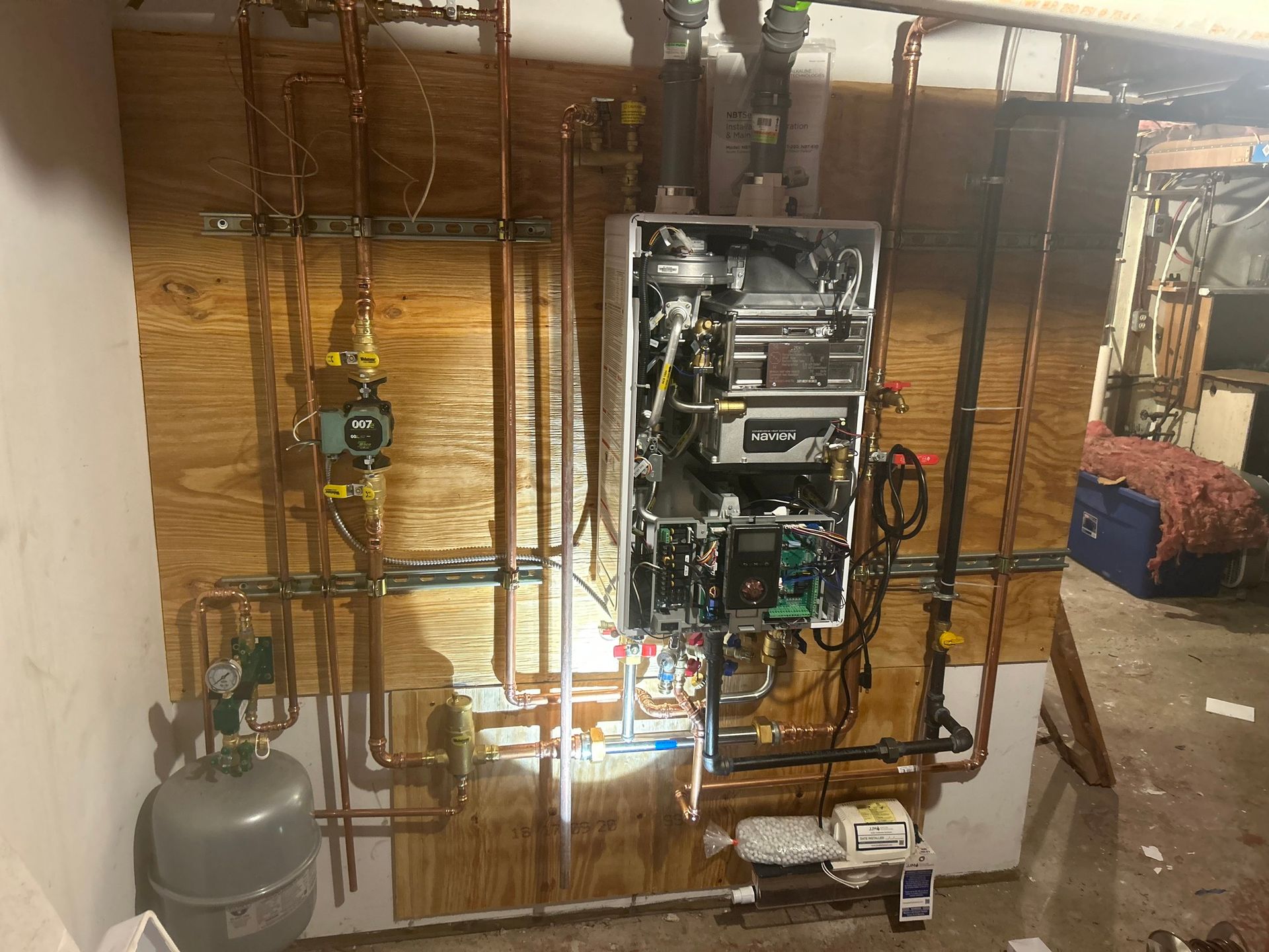 A boiler is being installed in a basement with copper pipes.