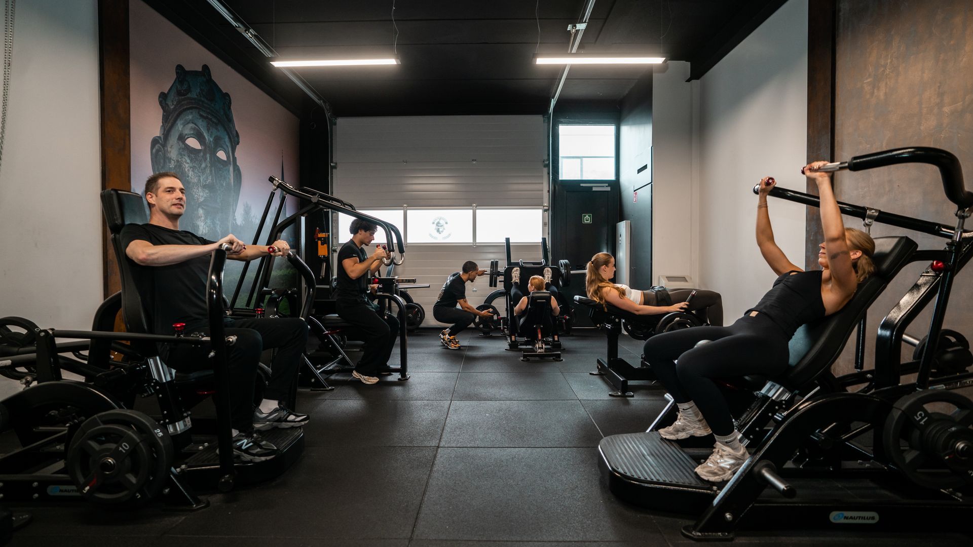 Een man zit op een machine in een sportschool terwijl een man achter hem staat.