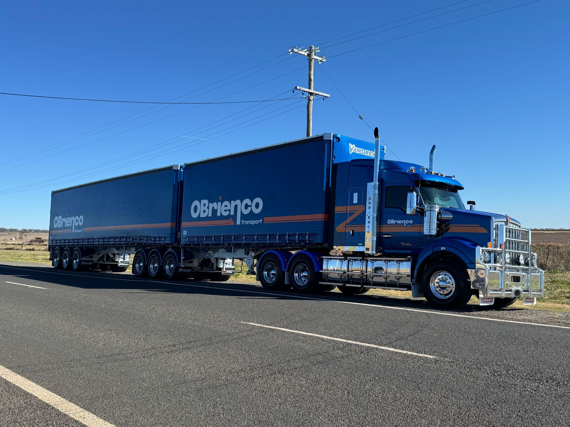 Blue semi-trailer truck with OBrienco branding parked on a road under a blue sky.