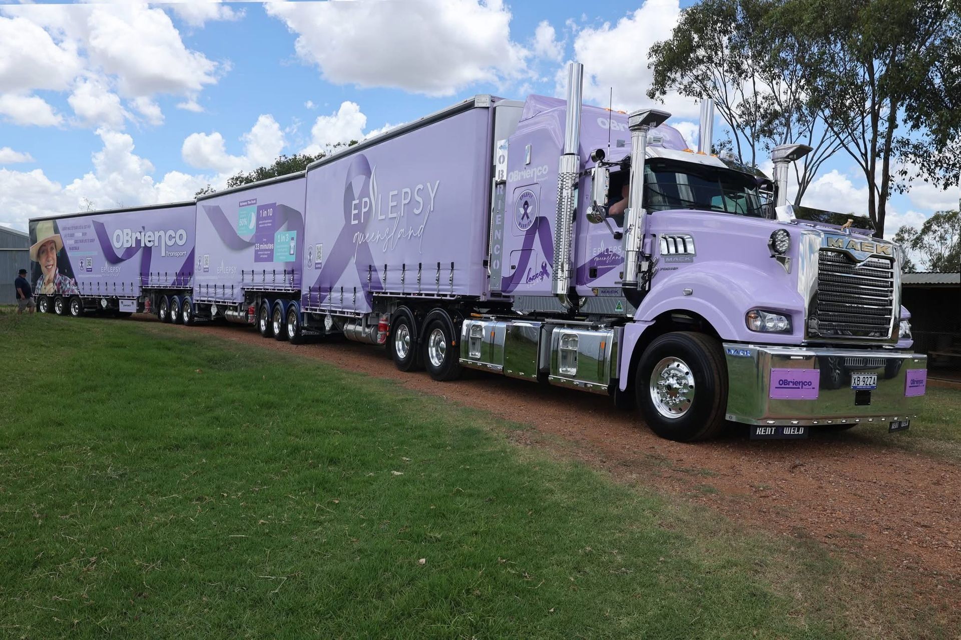 A lavender triple-trailer truck with chrome accents parked on dirt.