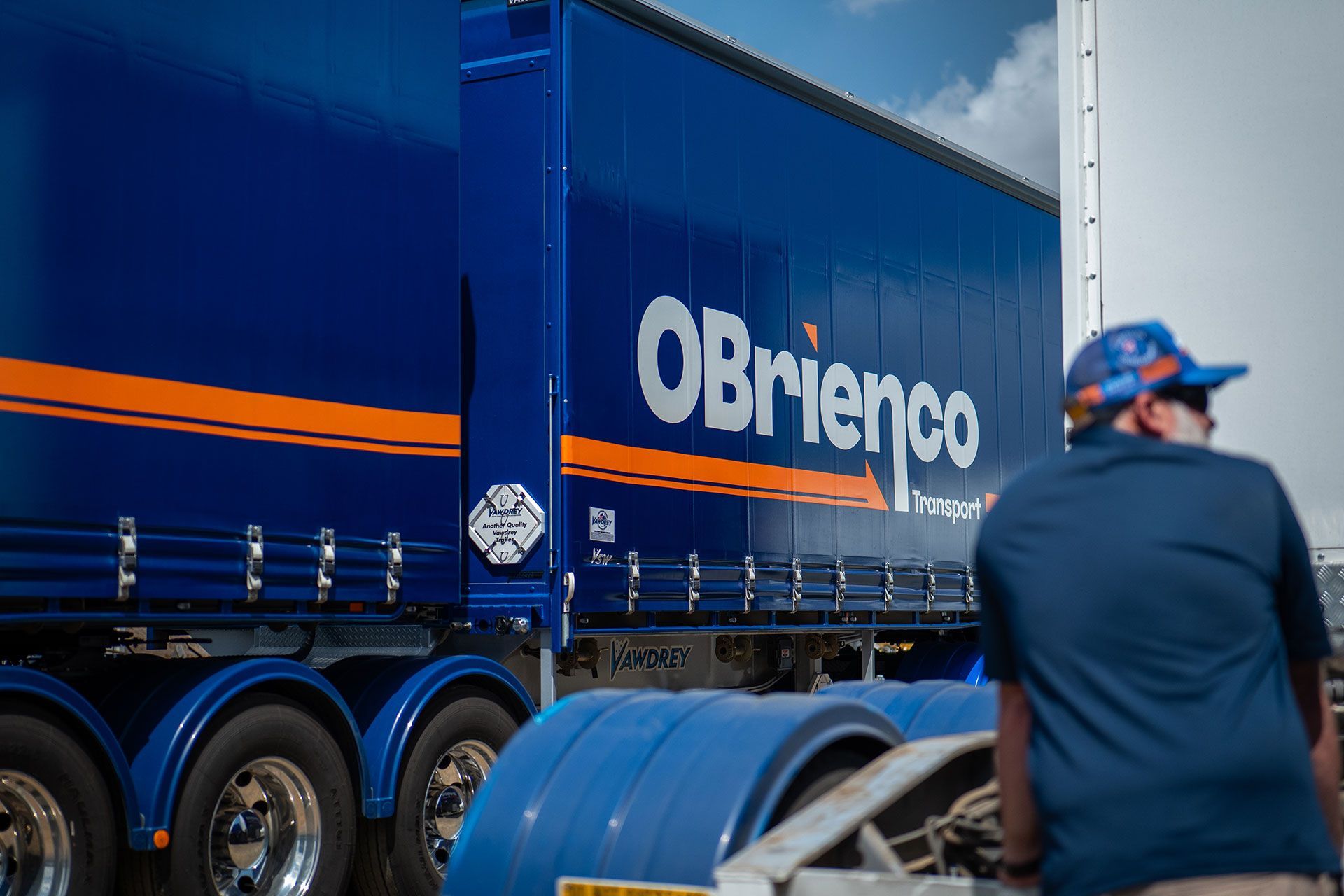 Blue O'Brienco transport semi-trailer with orange stripes, a person is visible in the foreground.