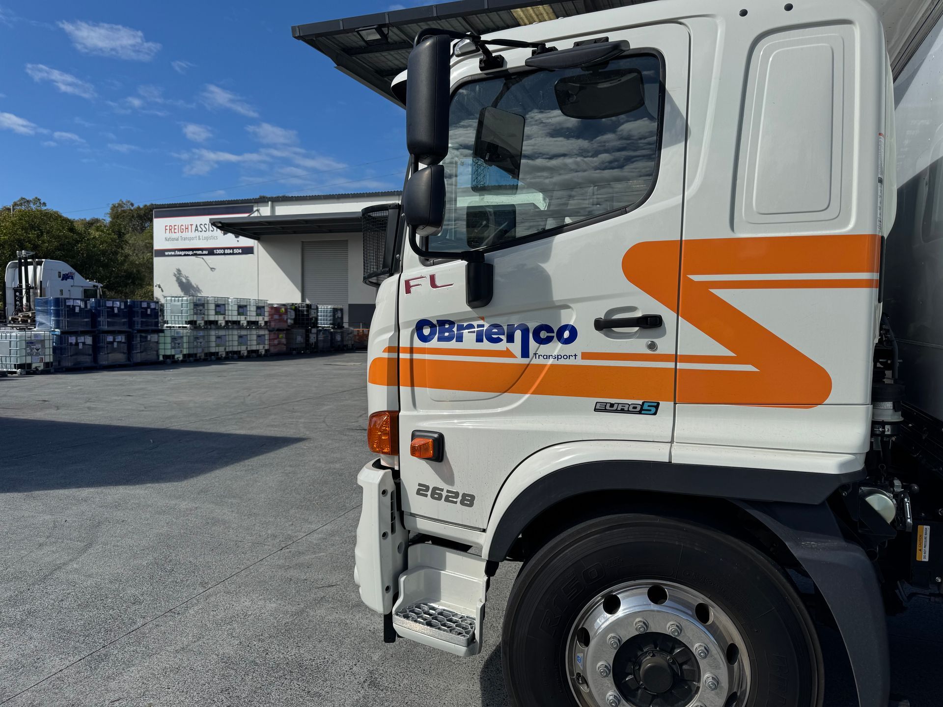 White and orange OBrienco truck parked outside a warehouse on a sunny day.