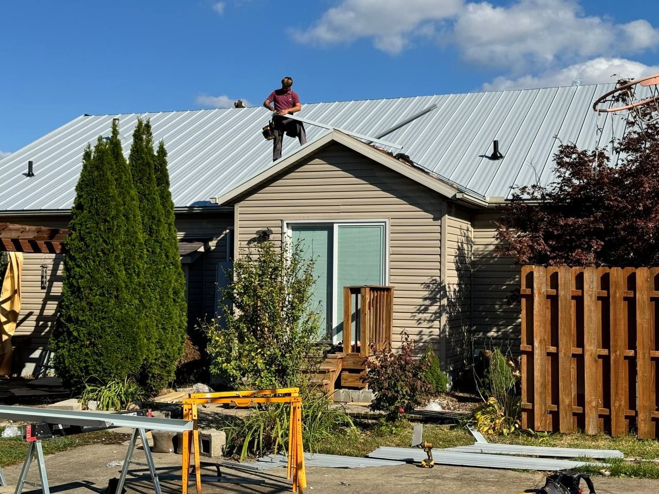 A blue roofing truck is parked in front of a house