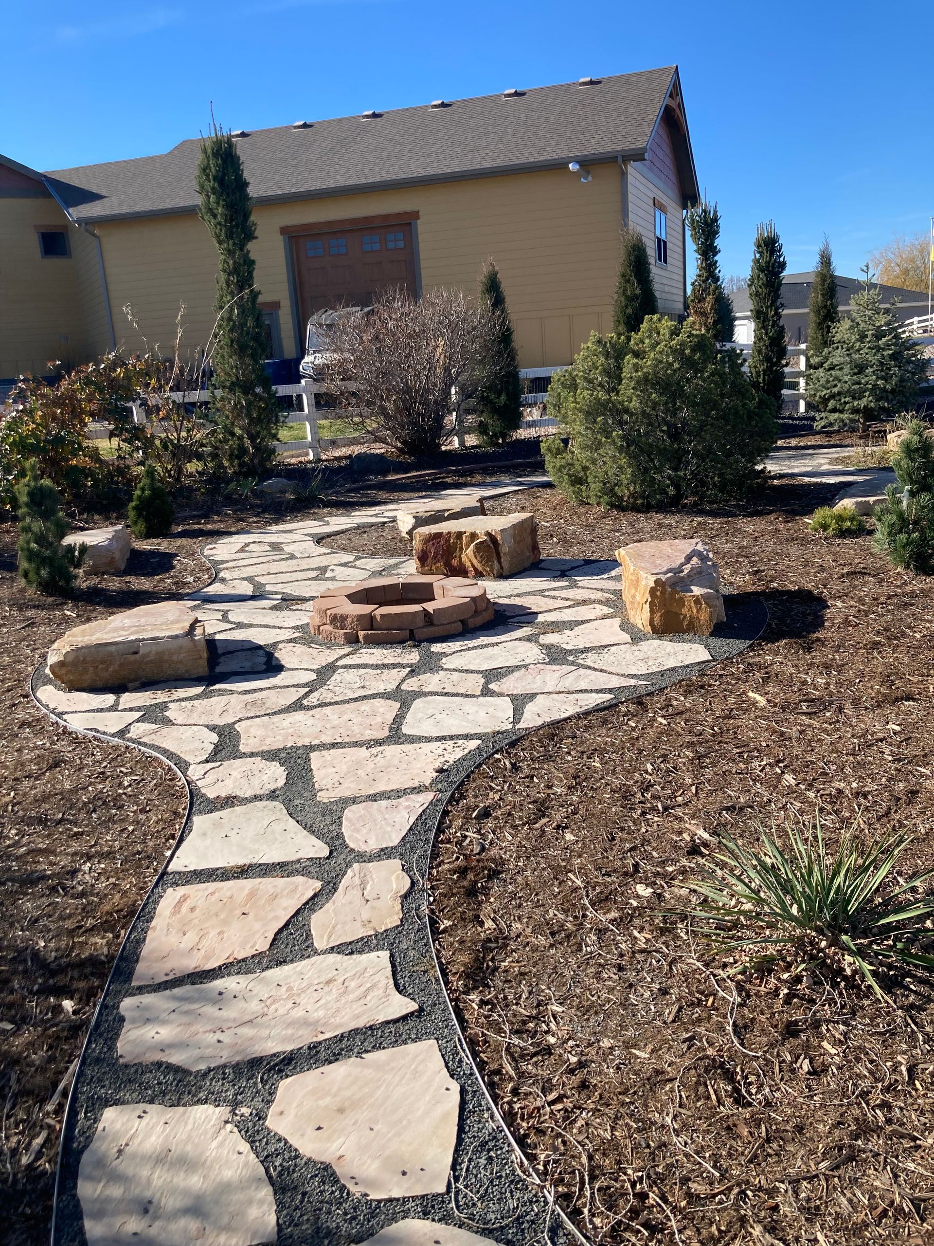 A stone walkway leading to a fire pit in front of a house.