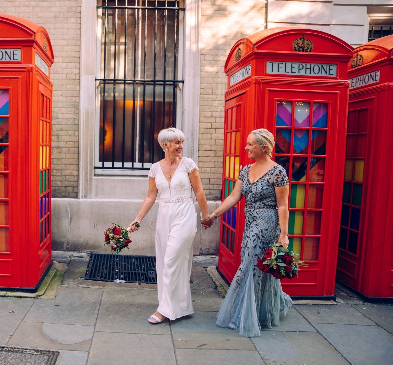Two women holding hands in front of red telephone booths