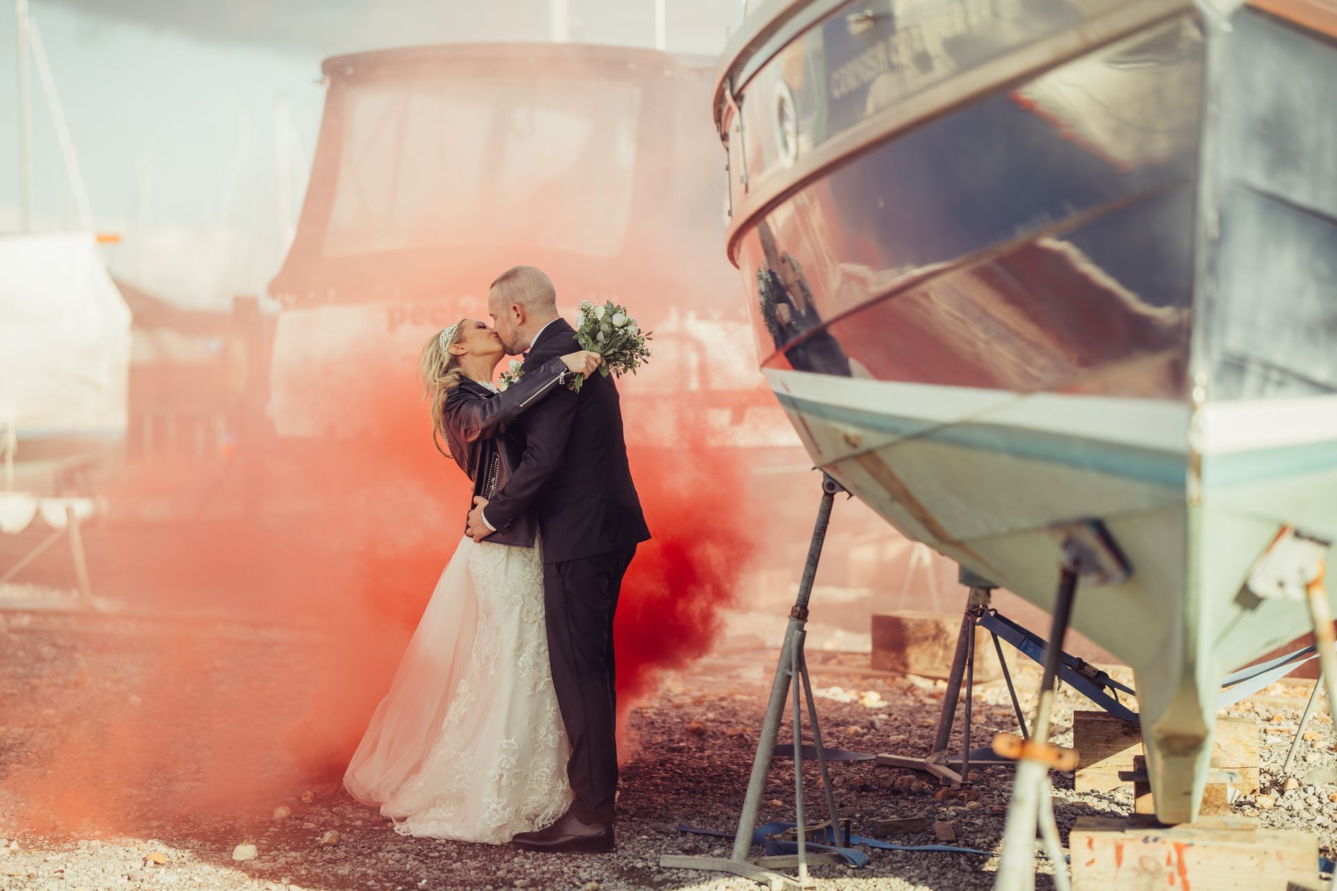 A bride and groom kissing in front of a boat with red smoke coming out of it.