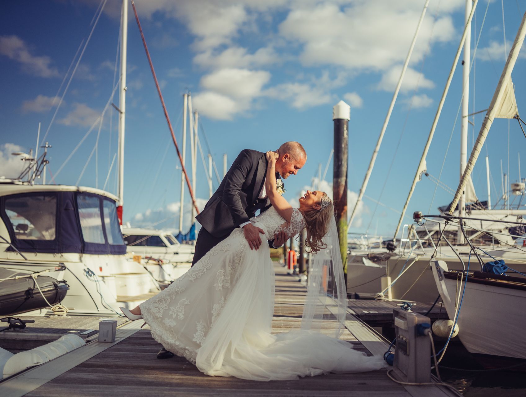 A bride and groom are kissing on a dock surrounded by boats.