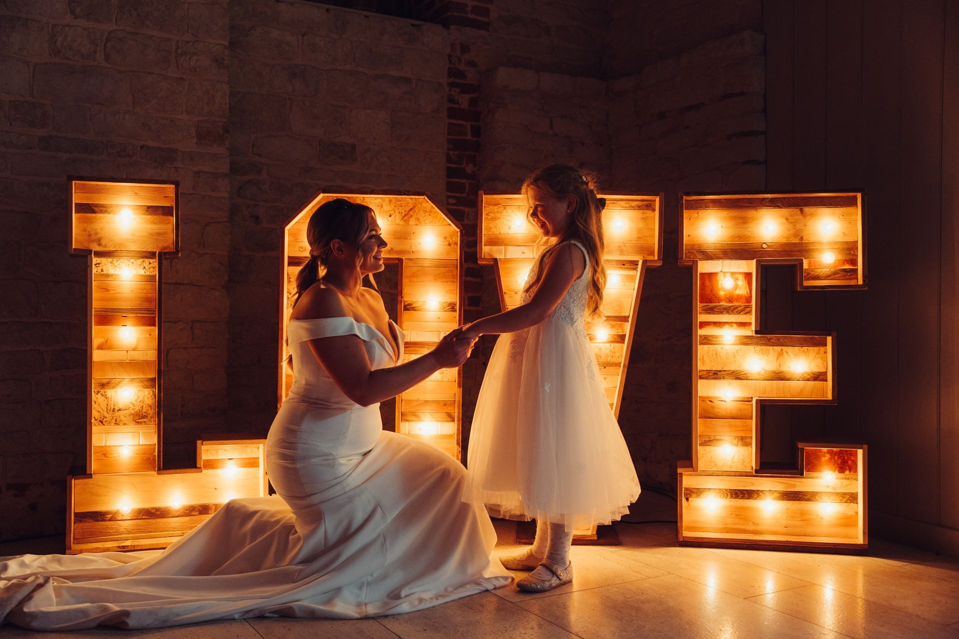 A bride and a flower girl are holding hands in front of a love sign.