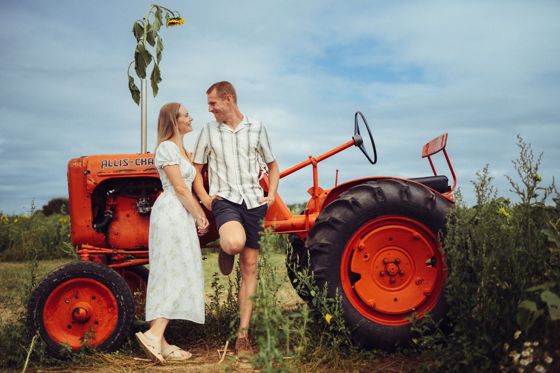 A man and a woman are standing next to an orange tractor in a field.