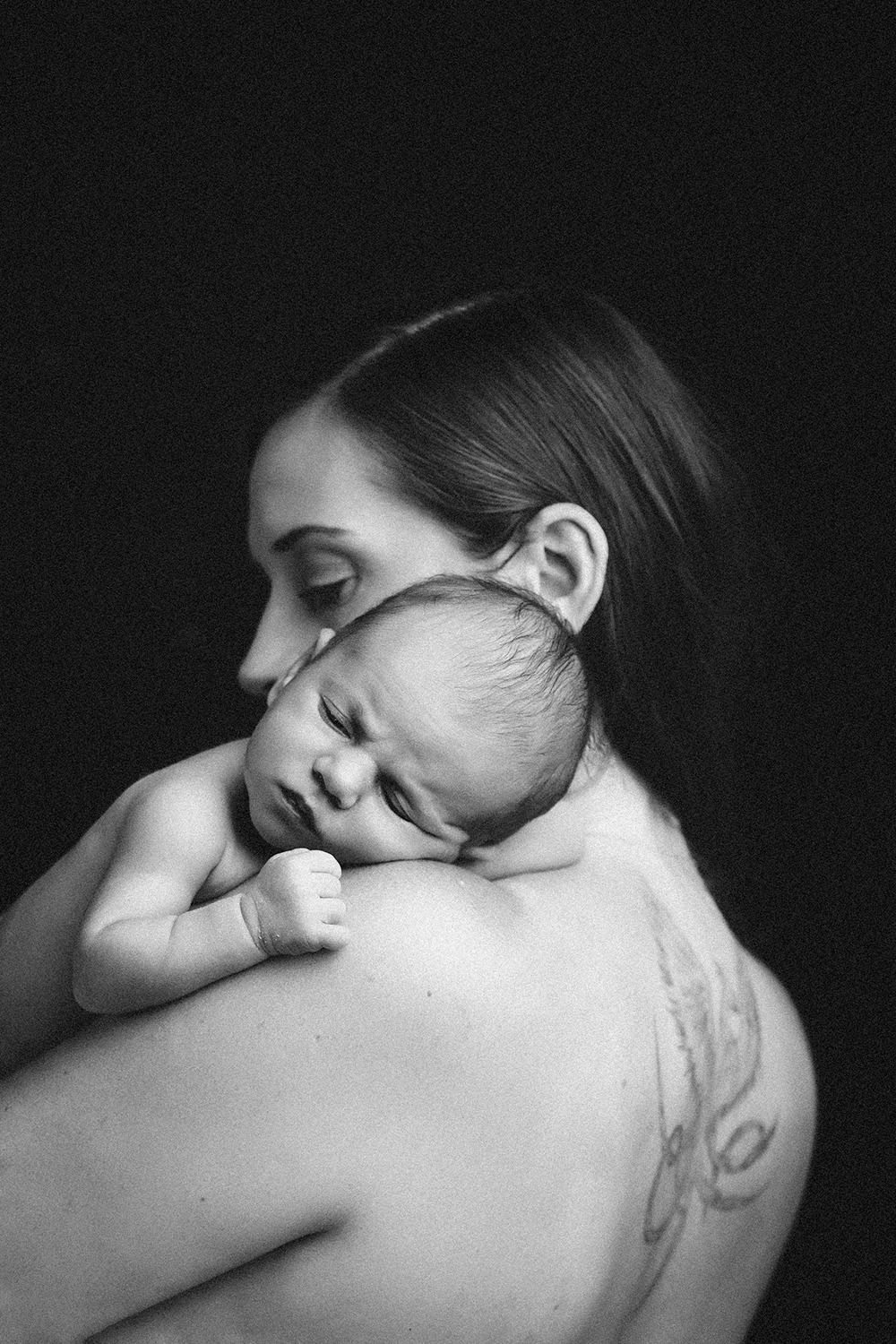 A woman is holding a baby on her shoulder in a black and white photo.