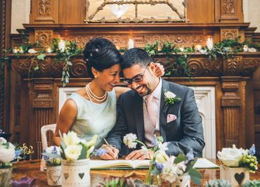A bride and groom are sitting at a table signing a wedding certificate.