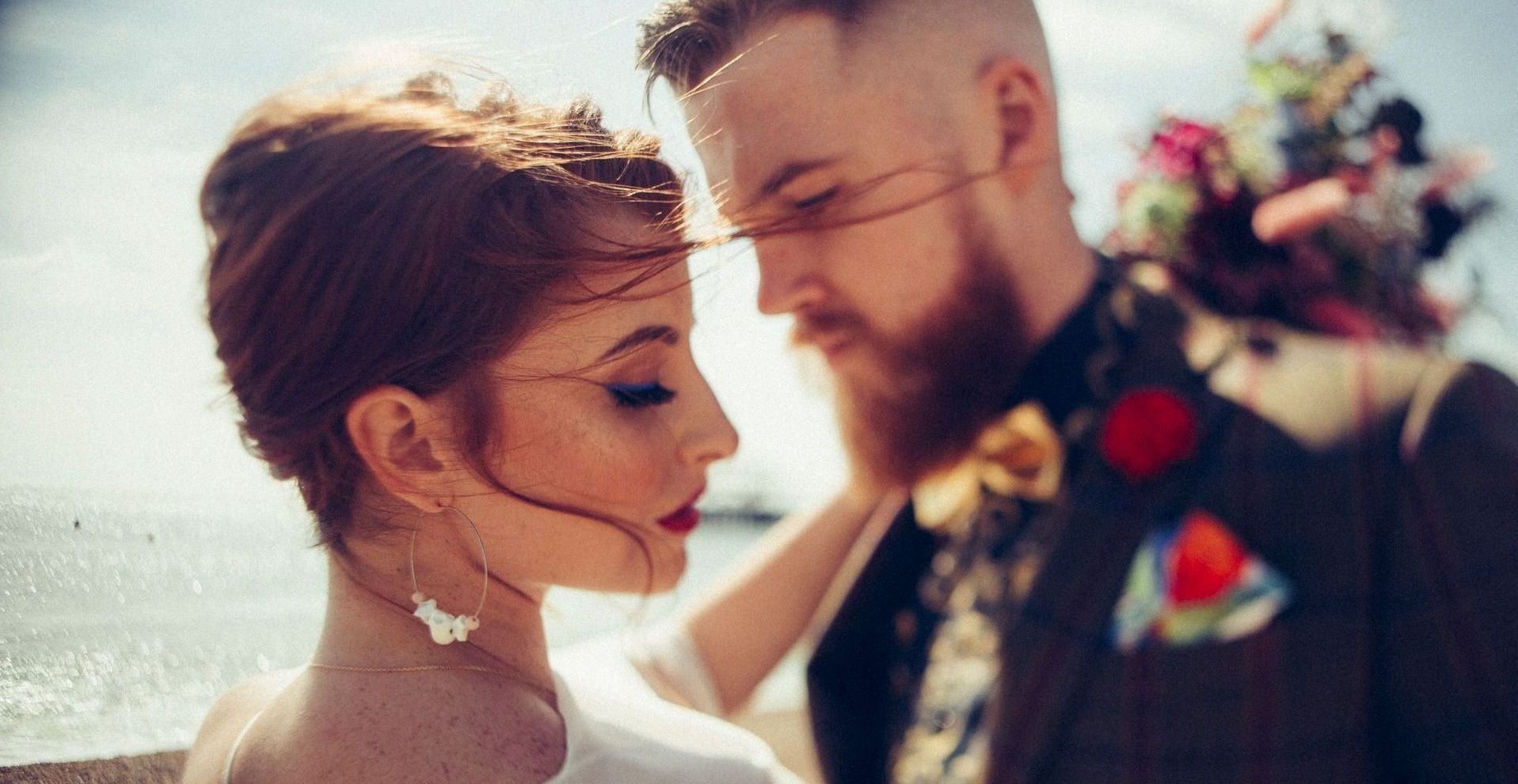 A bride and groom are looking at each other in front of the ocean.