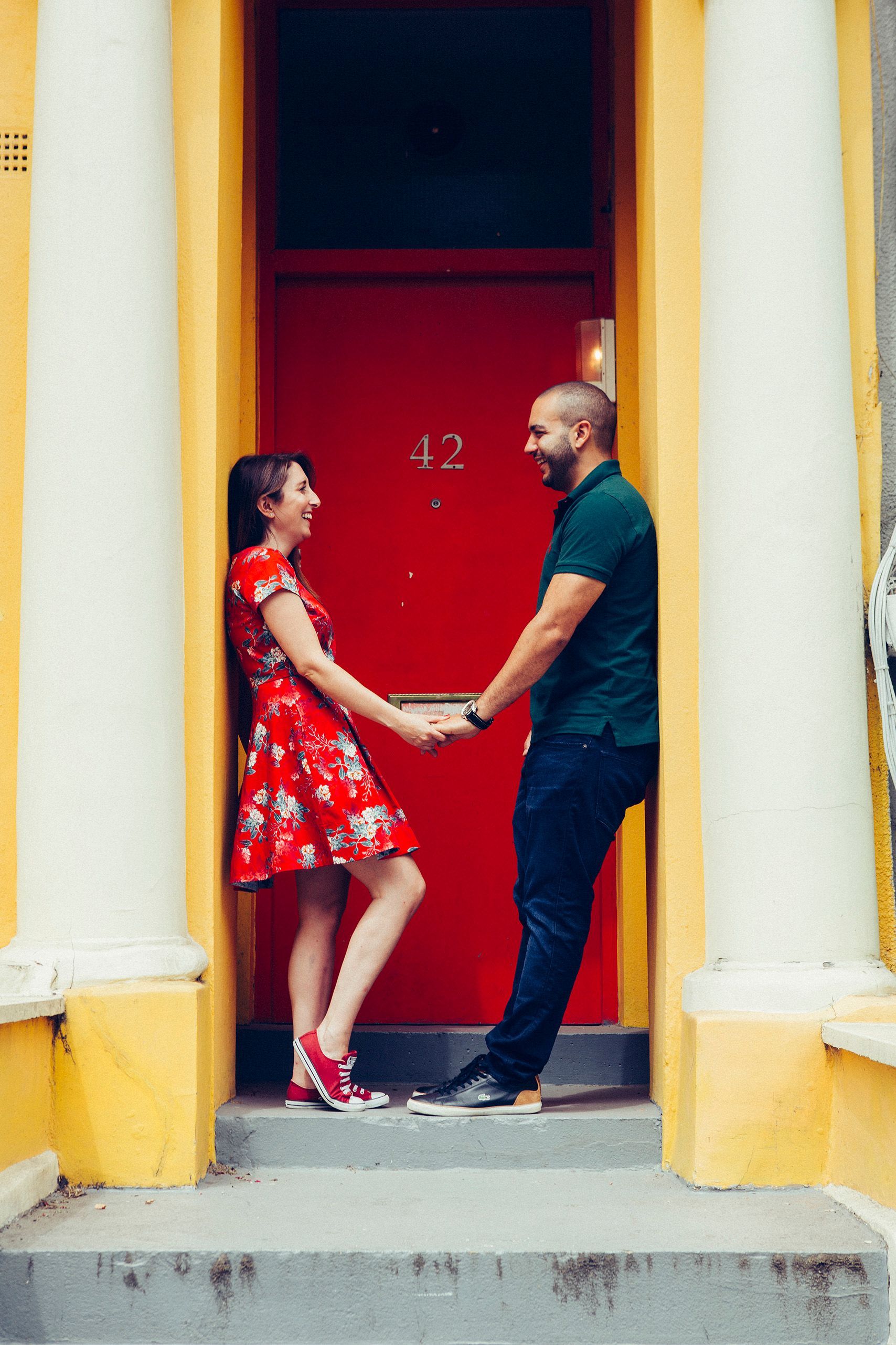 A man and a woman are holding hands in front of a red door.