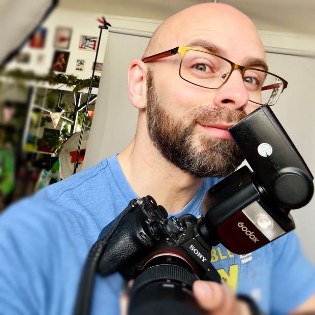 A bald man wearing glasses is holding a sony camera