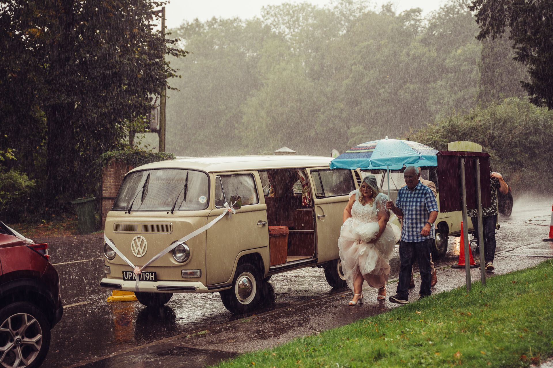 A bride and groom are walking towards a van in the rain.