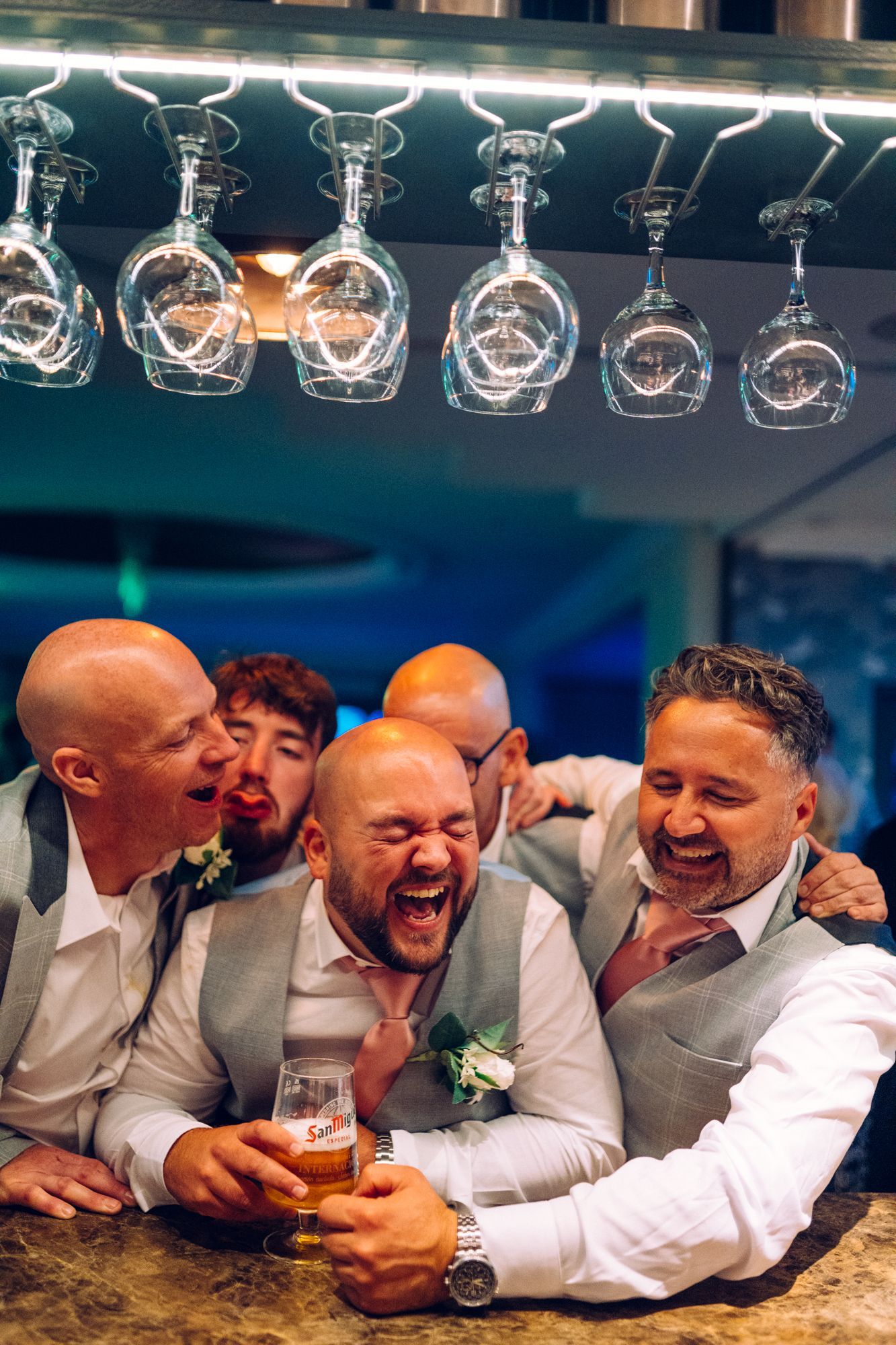 A group of men are laughing and drinking beer at a bar.