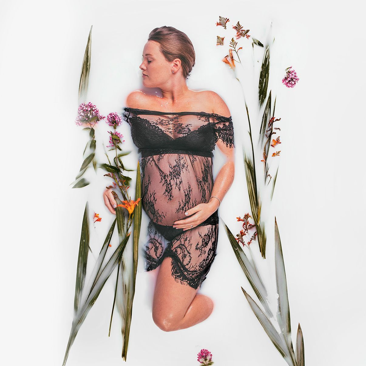 A pregnant woman is laying in a bathtub surrounded by flowers.