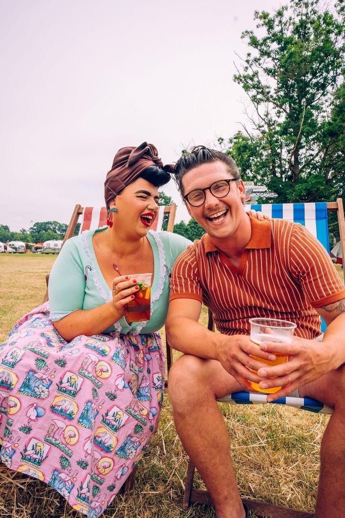 A man and a woman are sitting in lawn chairs drinking beer and laughing.