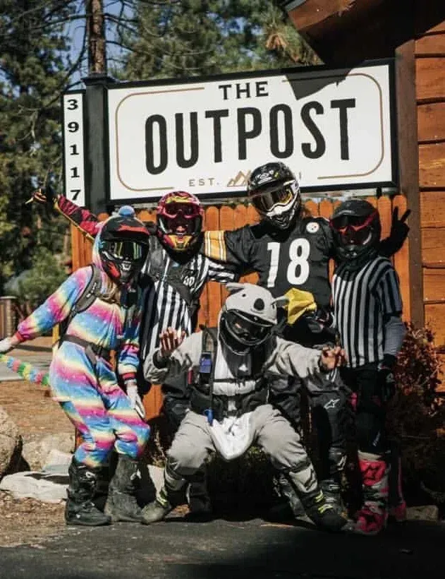 People in motorcycle gear pose in front of a building sign: 