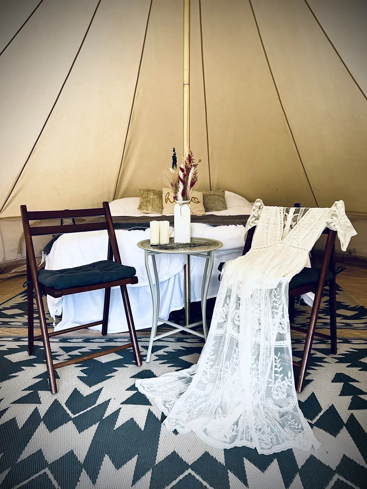 Glamping tent interior with bed, dress, table, chairs, and patterned rug.