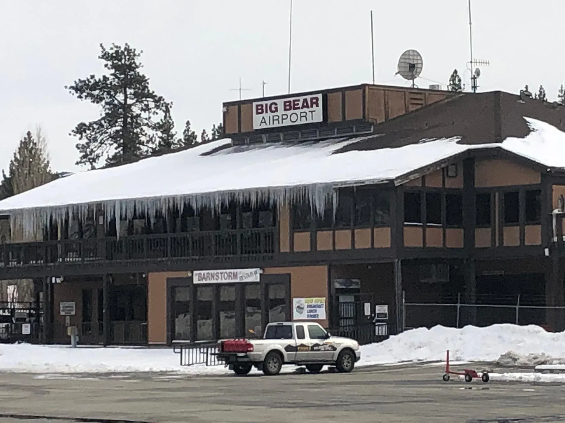 Big Bear Airport building with snow and icicles. A white pickup truck is parked in front.