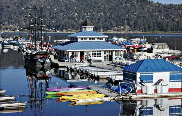 Marina on lake with blue buildings, boats, docks, and forested hills in background.
