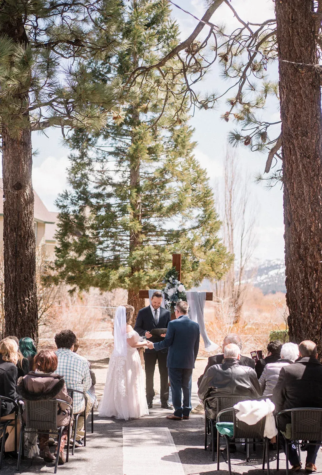 Wedding ceremony outdoors with couple, officiant, and guests seated in chairs.