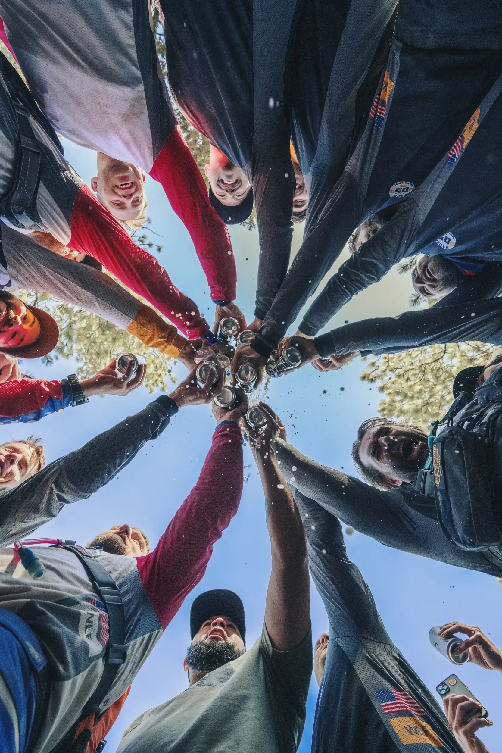 People in a circle, raising drinks in a toast; low-angle shot against a blue sky.