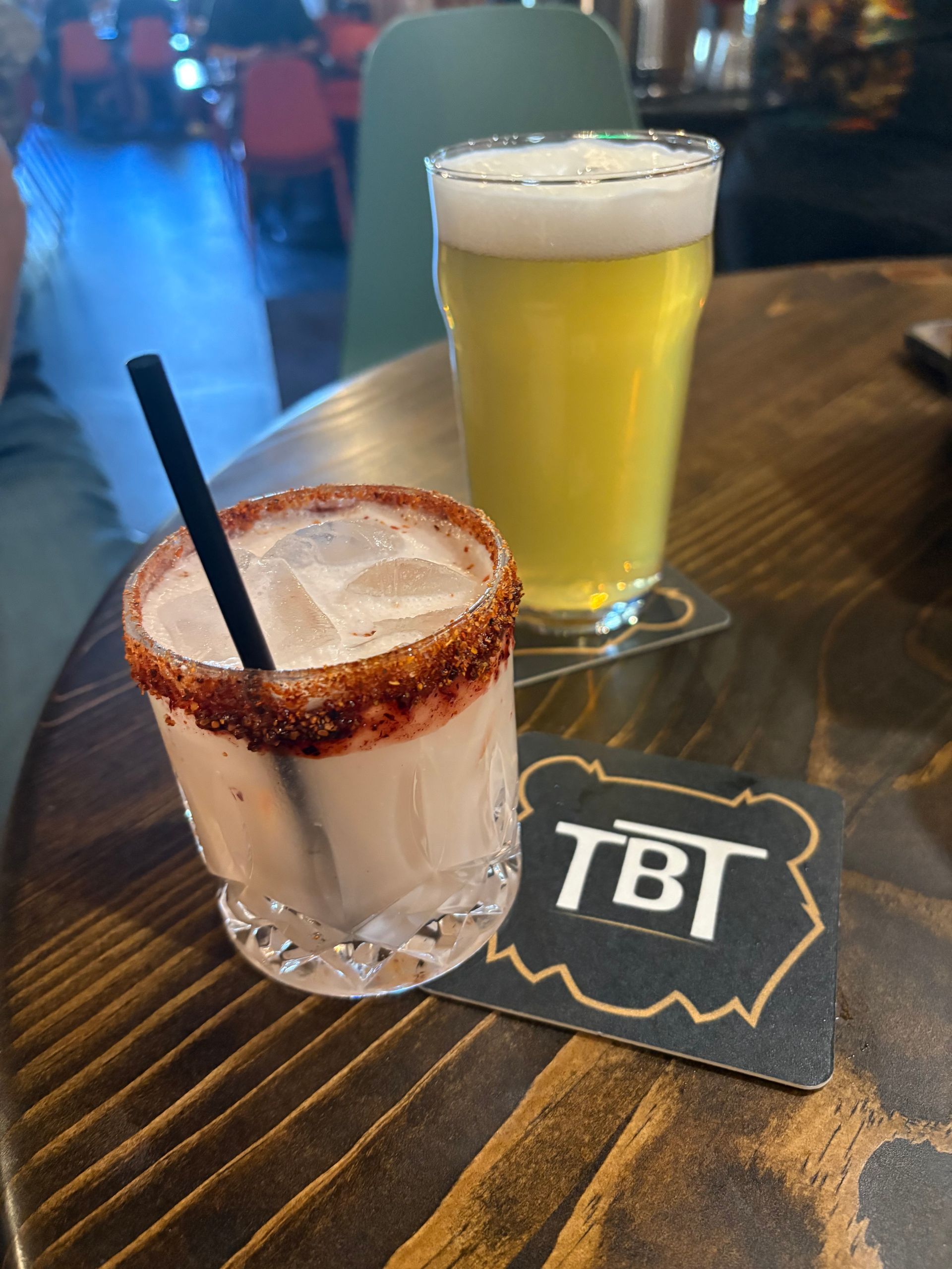 Exterior view of a green, rustic restaurant with outdoor seating under tall pine trees on a sunny day.
