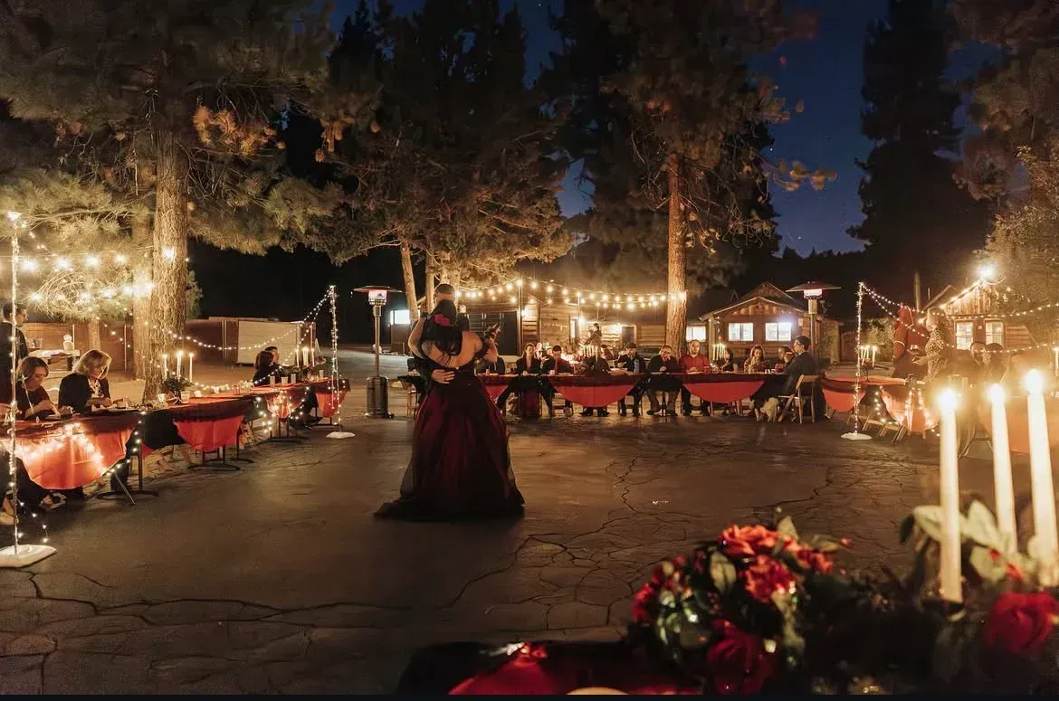 Couple dancing outdoors at night, surrounded by tables, string lights, and candles.
