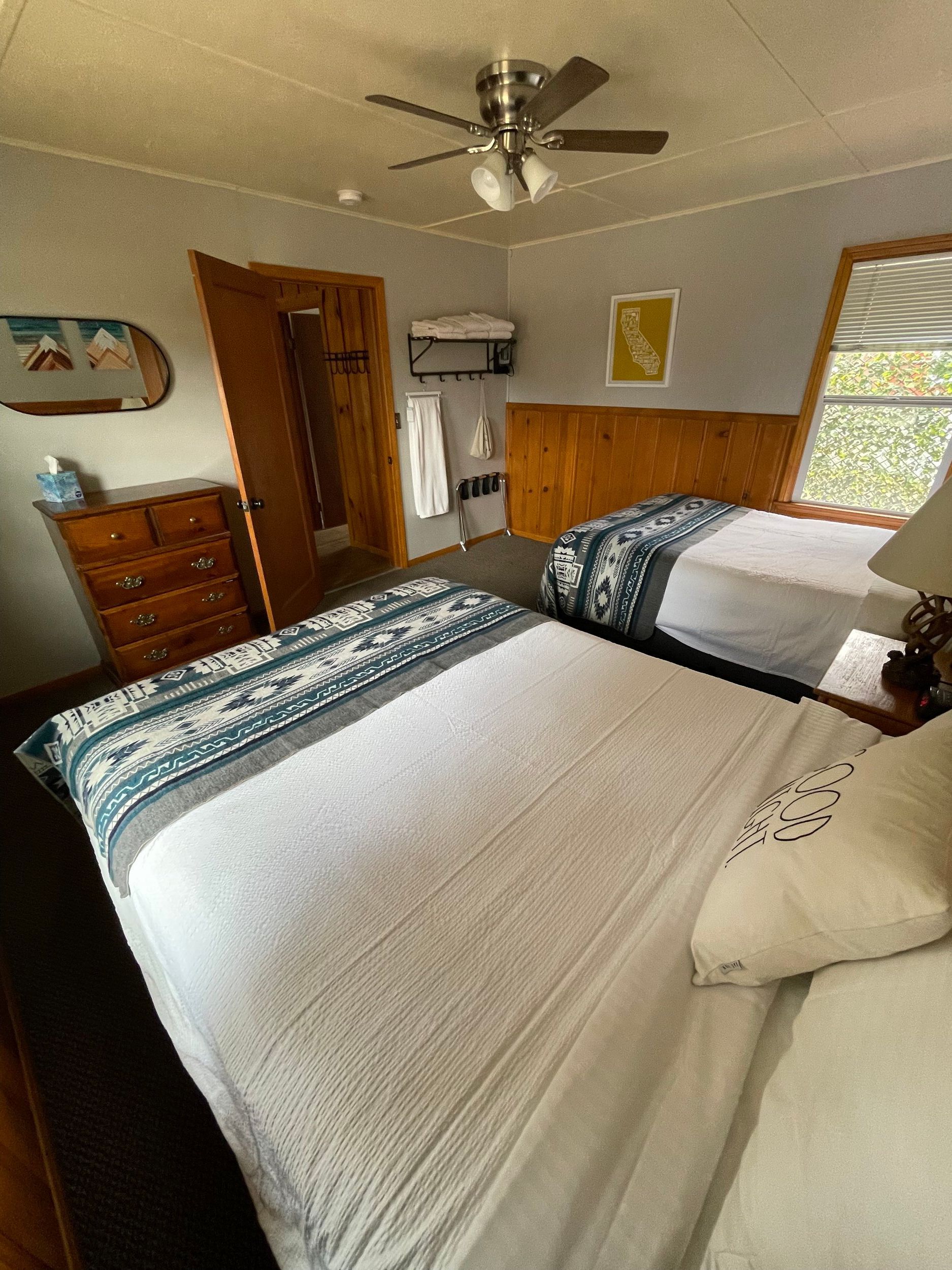 Bedroom with two beds, dresser, open closet, and window. Teal and white bedding. Ceiling fan.
