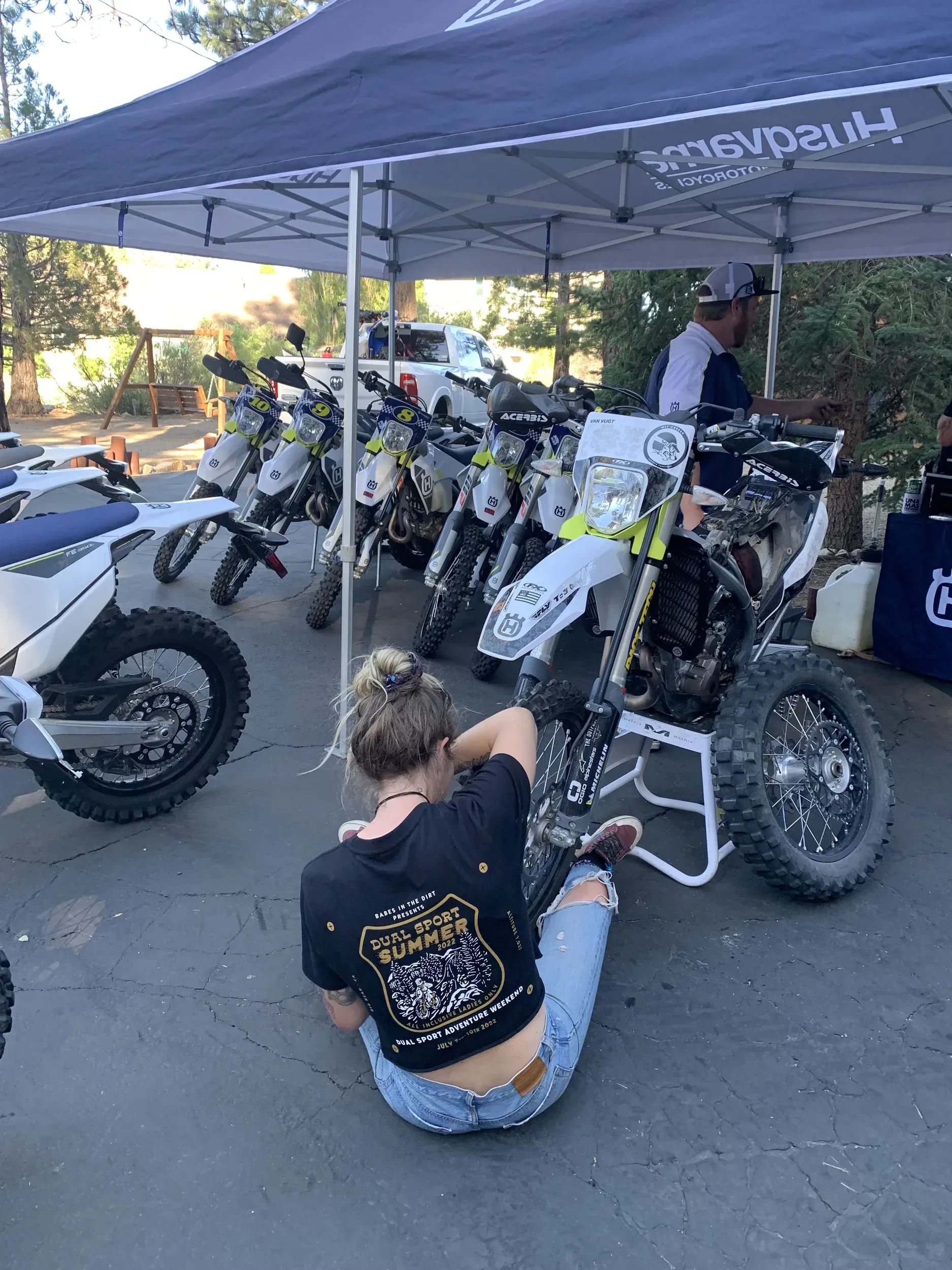 Woman looking at dirt bikes at an event booth; several Husqvarna motorcycles are on display.