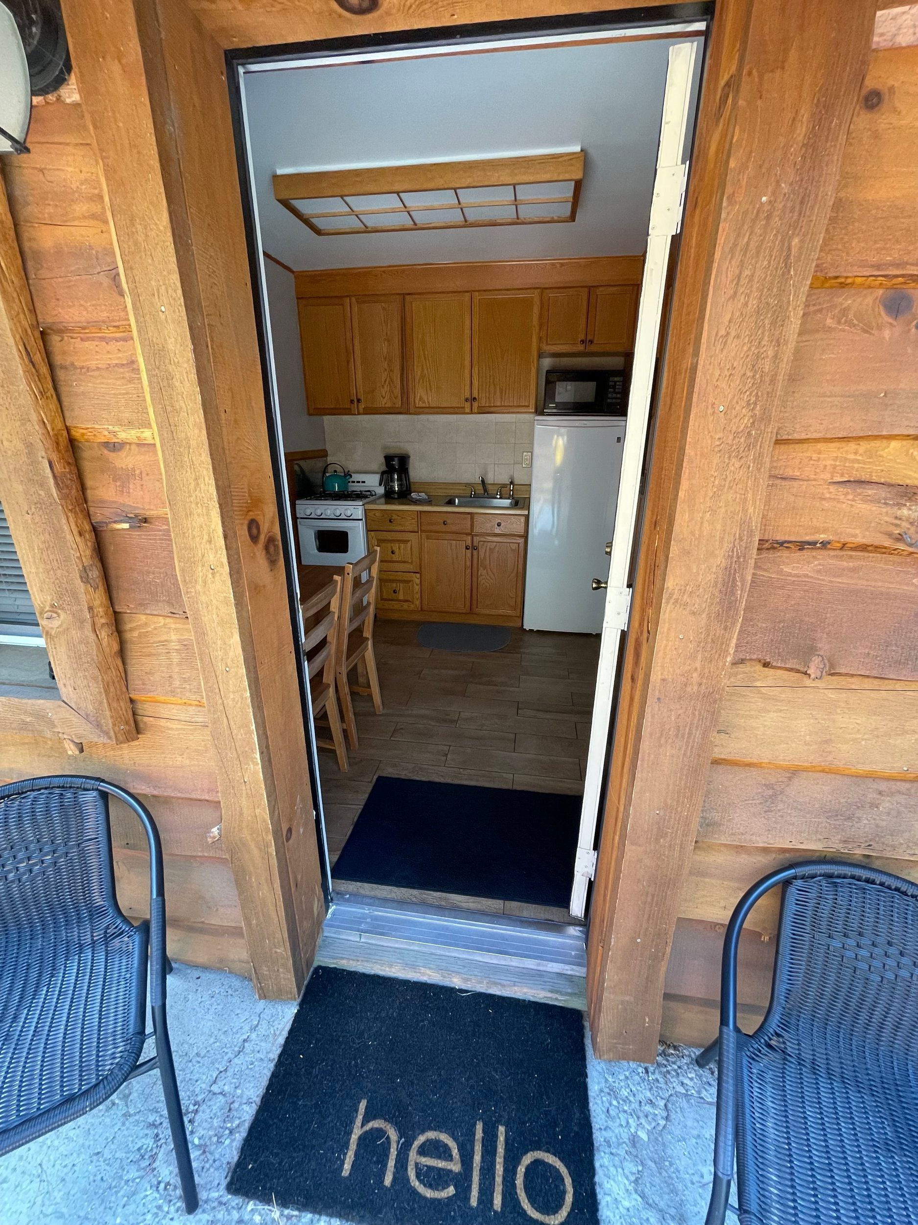 View of cabin doorway with welcome mat and interior kitchen visible.