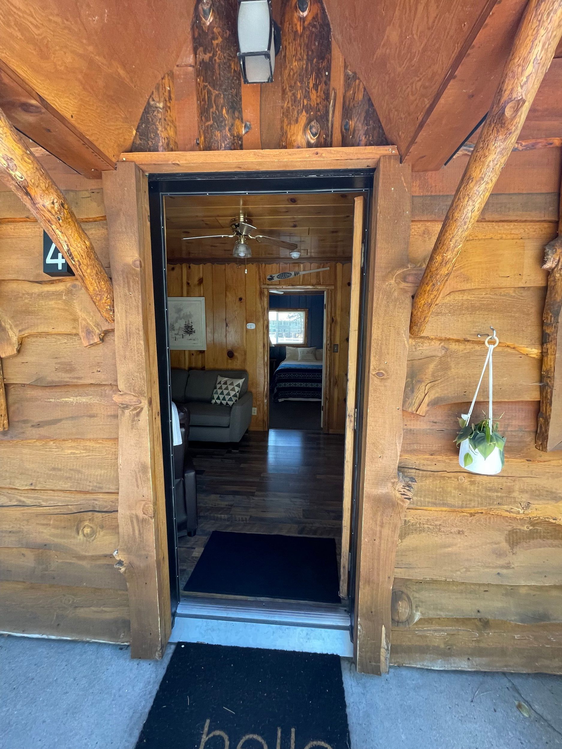 Wooden cabin doorway, open to a furnished interior. A black doormat reads 