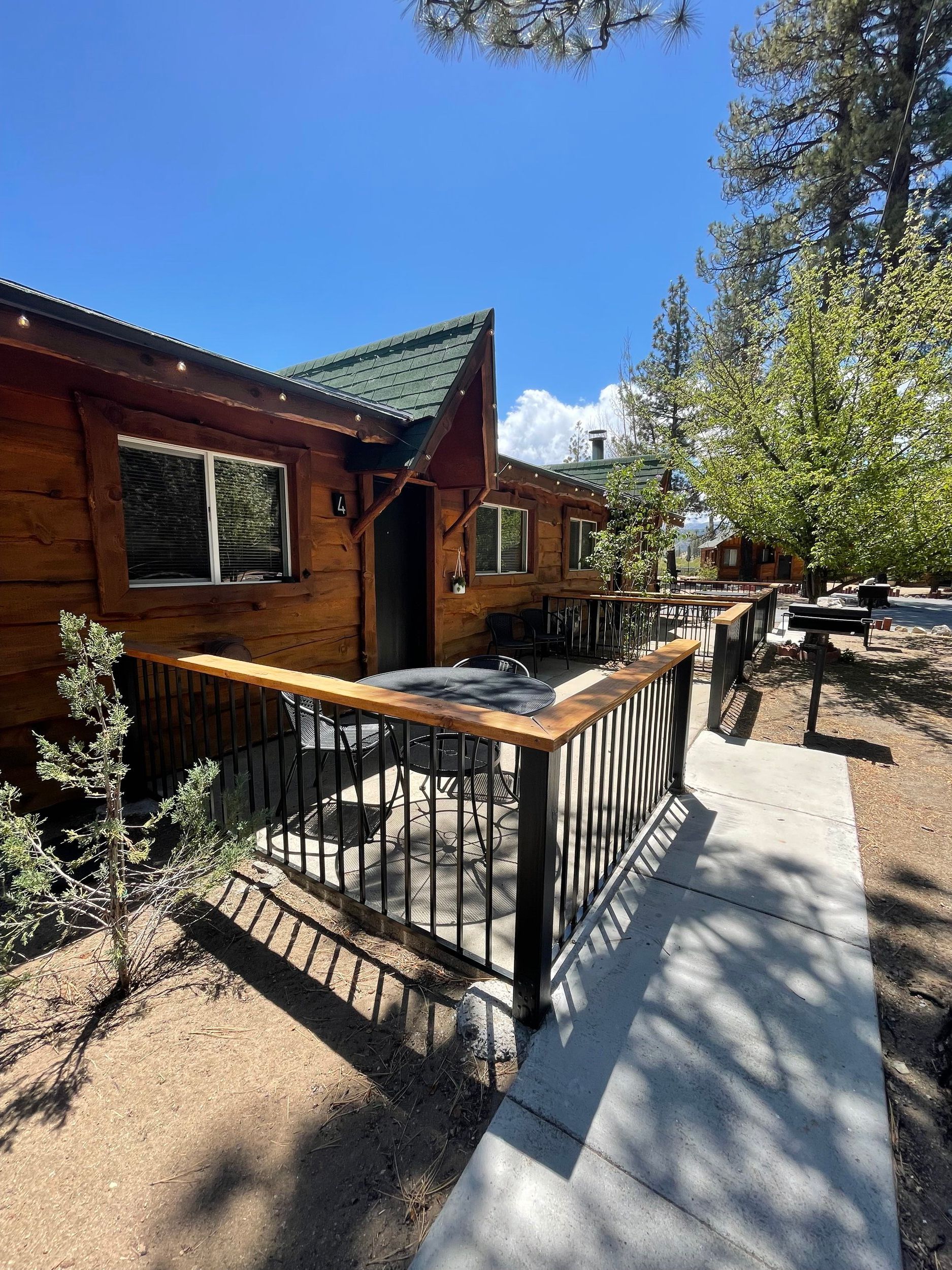Wooden cabin with railing, walkway, and trees under a blue sky.