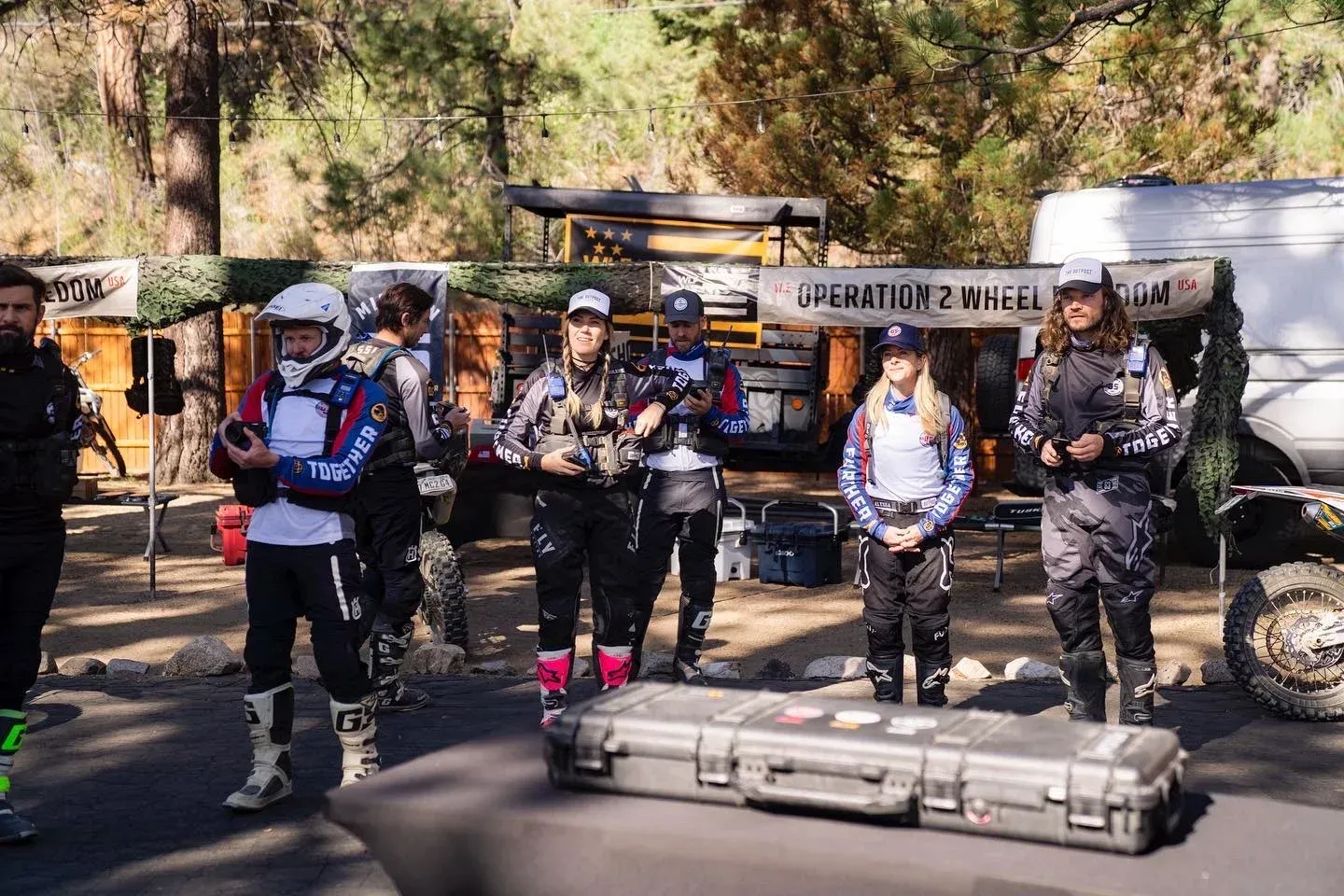 Group of people in motorcycle gear standing outdoors by a case.