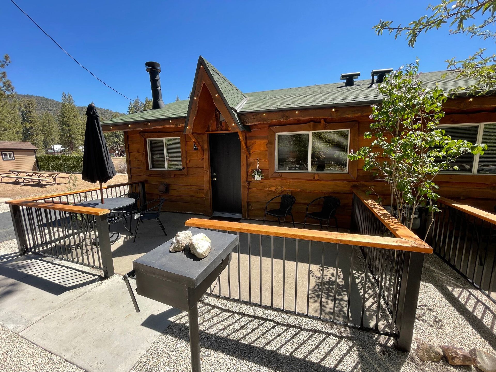 Cabin with a wooden facade, small patio, and outdoor seating. Blue sky.