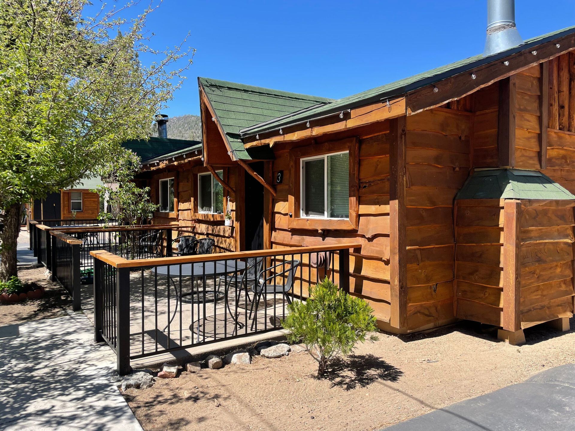 Wooden cabin with green roof and small porch, set against a bright blue sky.